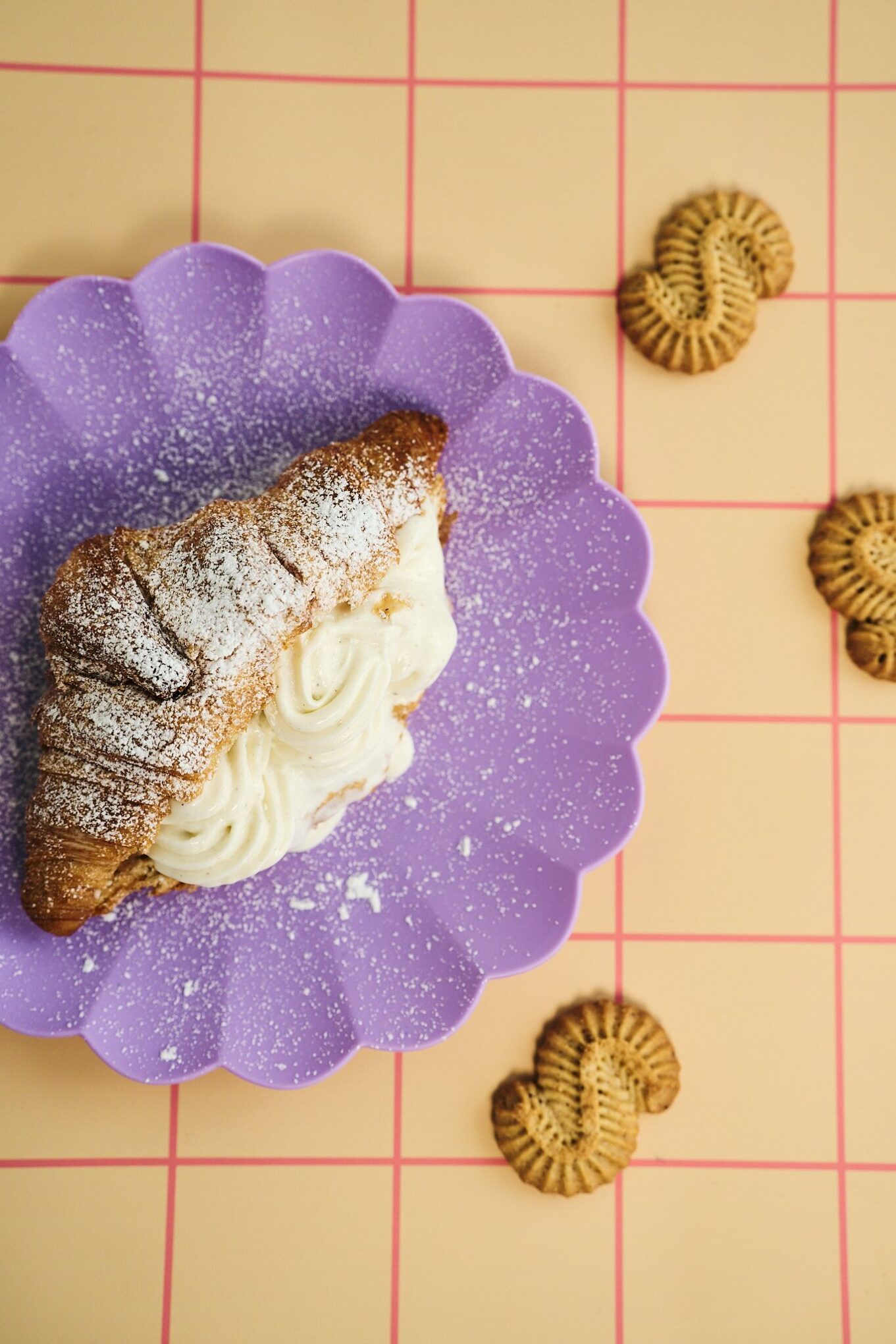 Täytetty croissant, jossa K. Leivon Leipomon kaneliässistä tehtyä kaneliässätahnaa ja jäätelöä, esillä pastellisessa kattauksessa.